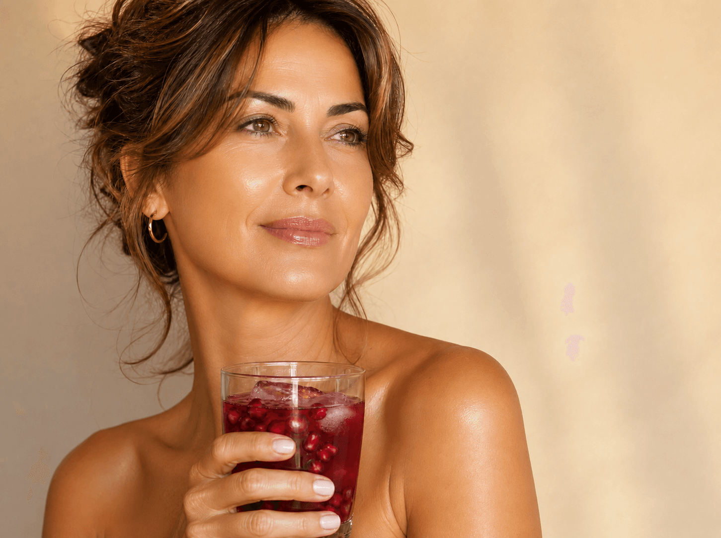 A woman holding a glass of pomegranate-red drink, looking toward the light.